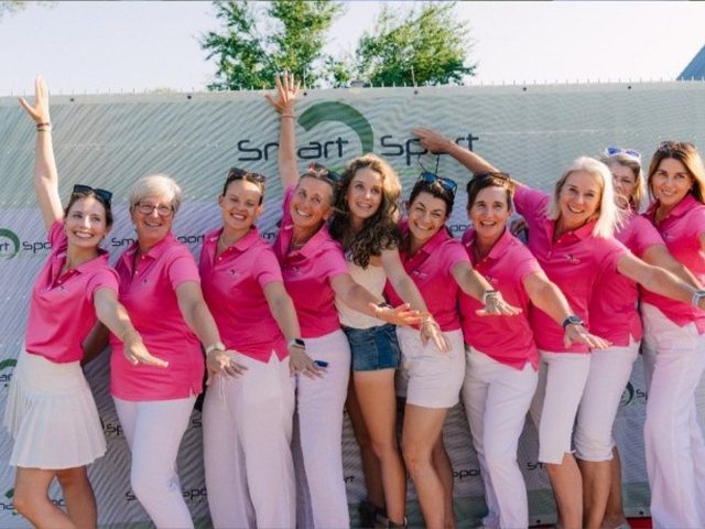 Die Damenmannschaft in pinken Poloshirts vor dem Banner von Smart Sport Reisen
